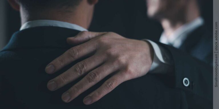 Kondolenz bei Kollegen - Mann legt seine Hand auf die Schulter eines anderen Mannes, um ihn zu trösten
