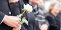 Trauergast in Schwarz hält eine weiße Rose